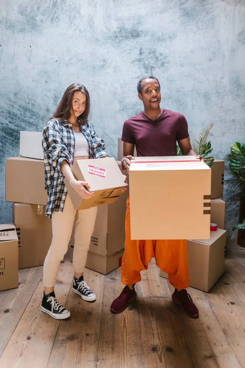 Two people carrying moving boxes into a new home